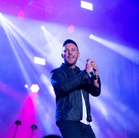 Picture of a man on stage with a microphone with purple lights.