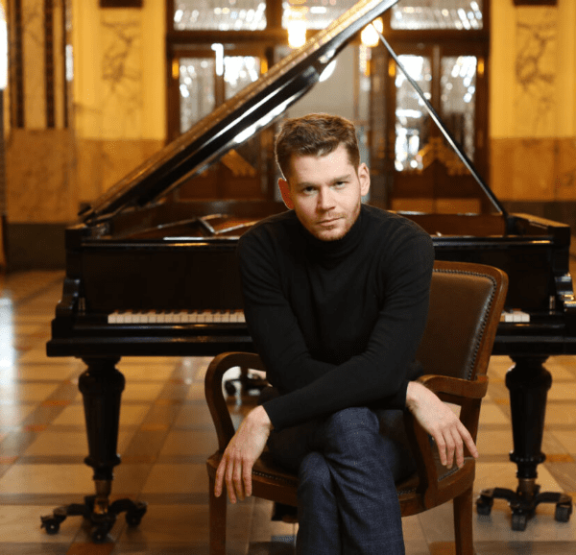 a man sitting in a chair with a grand piano behind him