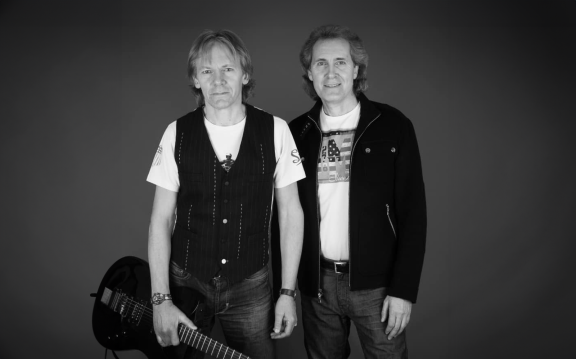 a black and white image of 2 men, one is holding a guitar
