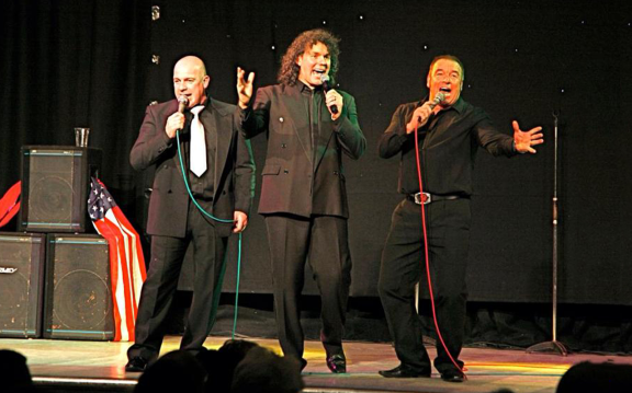 an image of 3 men singing on stage