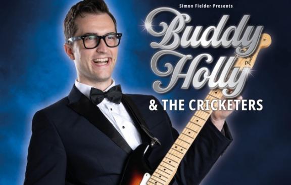man in suit playing a guitar with a blue background 
