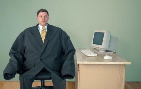 an image of a man sitting at a desk wearing a massive oversized suit