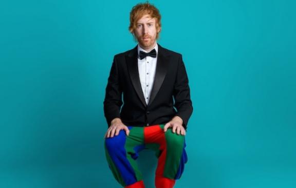 a man wearing a black tie suit on top and jester trousers