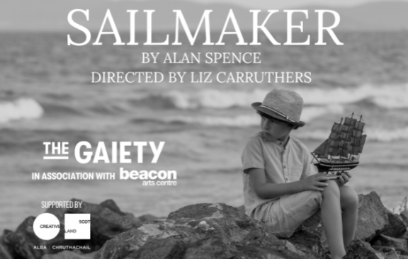 a boy sitting on rocks by the sea holding a model ship