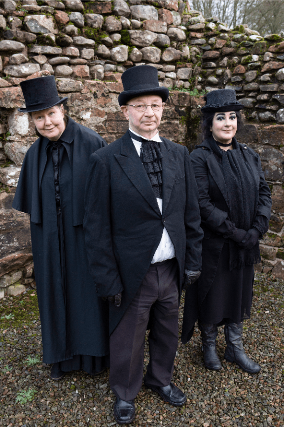 3 people stand by a wall wearing old fashioned black clothing