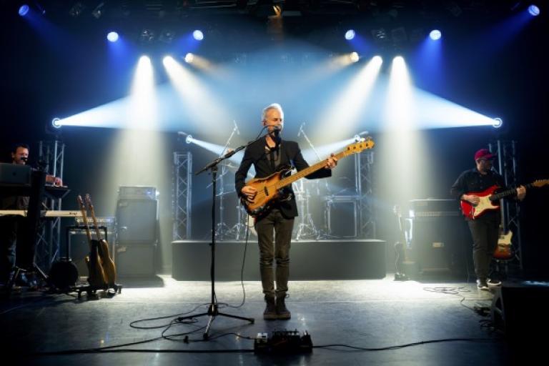 A man stands on stage with a guitar with spotlights on him.