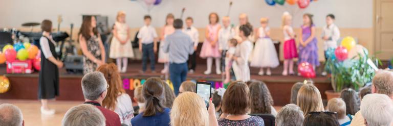 Child stand on a stage with balloons with an audience.