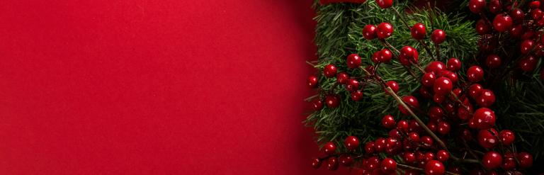 A green wreath with cranberries dotted on it with a red bow on a red background.