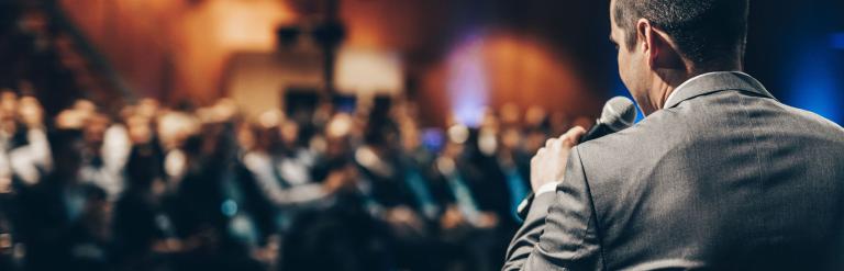 A man speaks in a microphone to an audience.