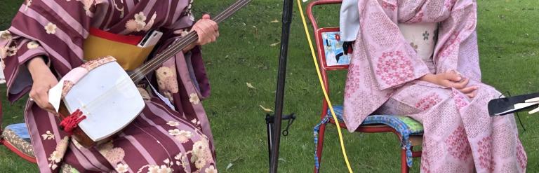 a woman and a girl in traditional Japanese clothing seated playing instruments